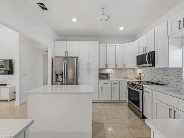 Kitchen with white cabinets, a center island, appliances with stainless steel finishes, decorative backsplash, and recessed lighting