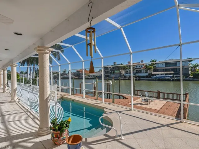 Swimming pool with a dock, glass enclosure, a sunroom, a water view, and a patio area