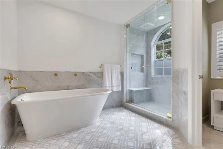 Bathroom featuring a marble finish shower, tile walls, a wainscoted wall, a freestanding tub, and vanity