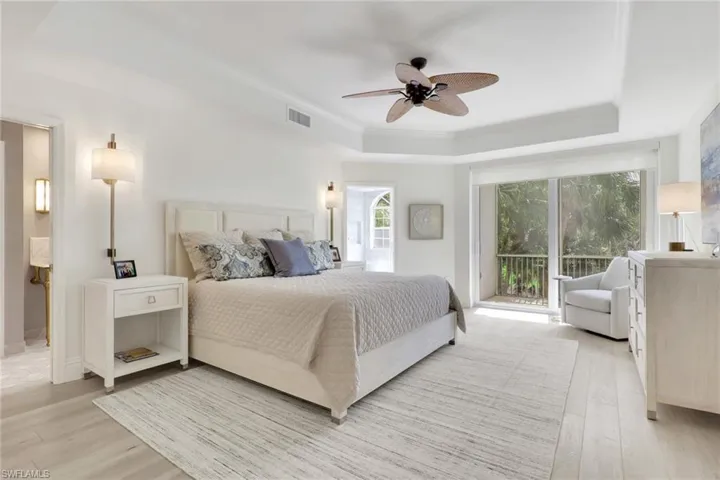 Bedroom with access to exterior, ceiling fan, real wood floors, a tray ceiling, and crown molding