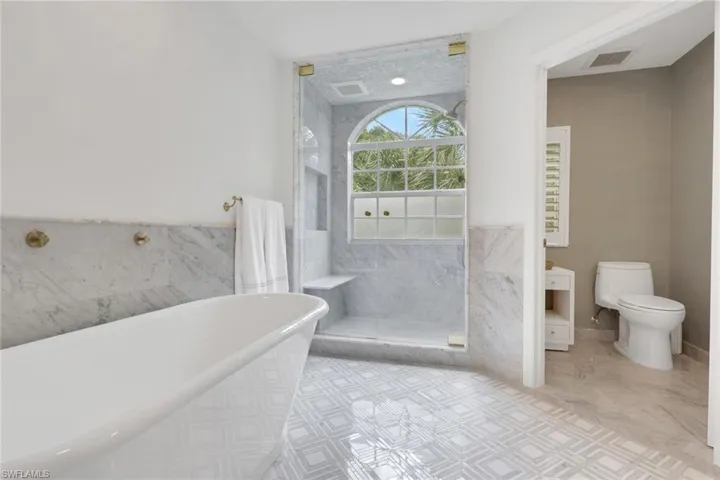 Bathroom featuring a freestanding tub, a marble finish shower, and tile walls