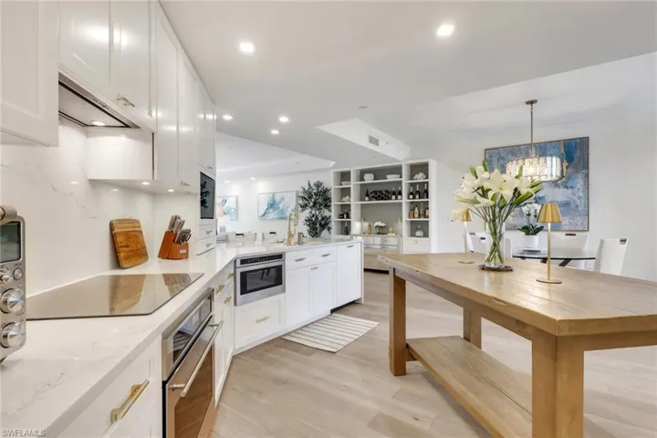 Kitchen featuring a peninsula, white cabinets, real wood flooring, hanging light fixtures, and oven