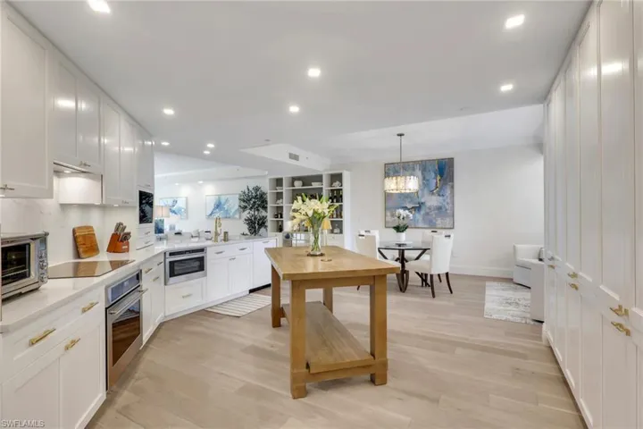 Kitchen with white cabinets, pendant lighting, real wood flooring, stainless steel appliances, and light stone counters