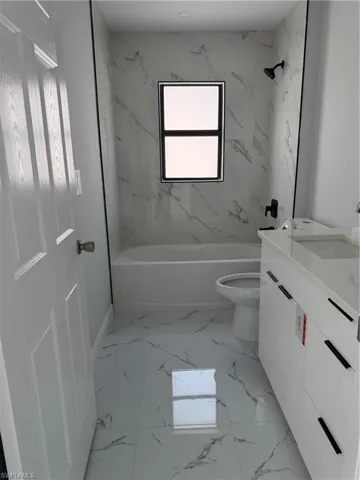 Full bath featuring vanity, shower / bath combination, and light marble finish flooring