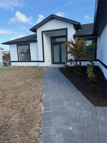 View of front of home featuring decorative driveway, stucco siding, roof with shingles, and a front yard