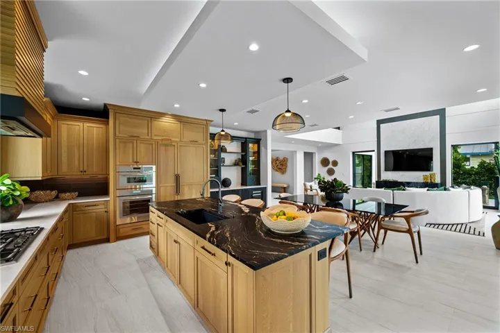 Kitchen featuring a kitchen island with sink, stainless steel appliances, recessed lighting, hanging light fixtures, and wall chimney range hood