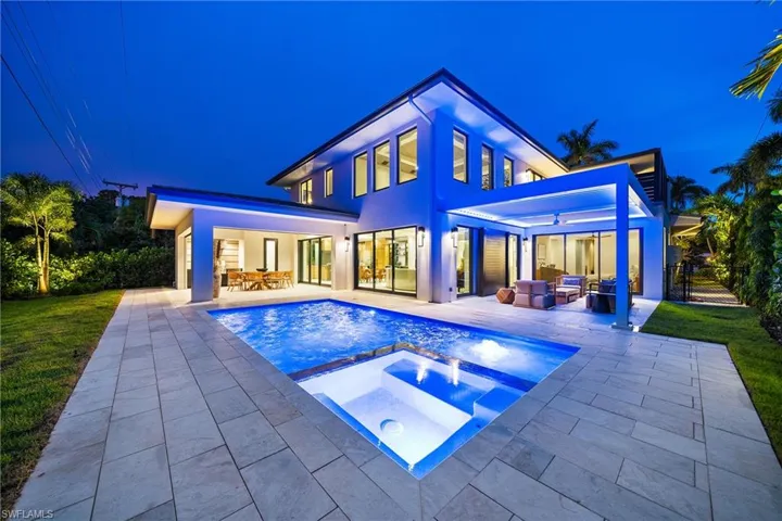 Back of house at night with an outdoor hangout area, a patio, a pool with connected hot tub, and a yard