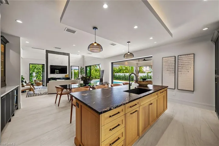 Kitchen featuring recessed lighting, a center island with sink, pendant lighting, glass insert cabinets, and dark stone counters