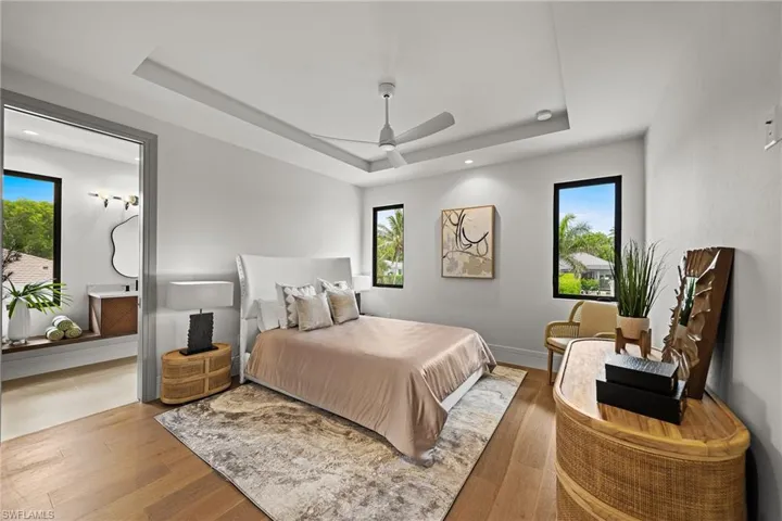Bedroom featuring a tray ceiling, multiple windows, wood finished floors, ceiling fan, and recessed lighting