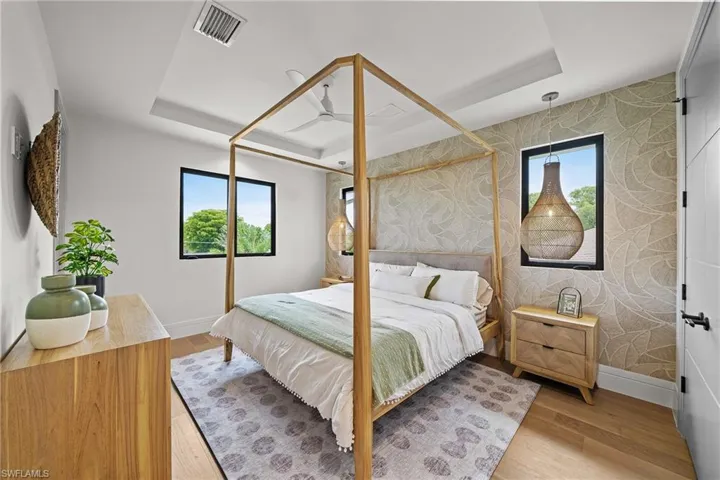 Bedroom featuring a tray ceiling, multiple windows, and wood finished floors