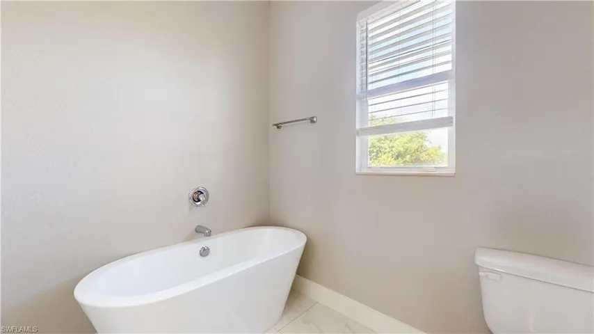 Bathroom with a freestanding tub, toilet, baseboards, and marble finish floors