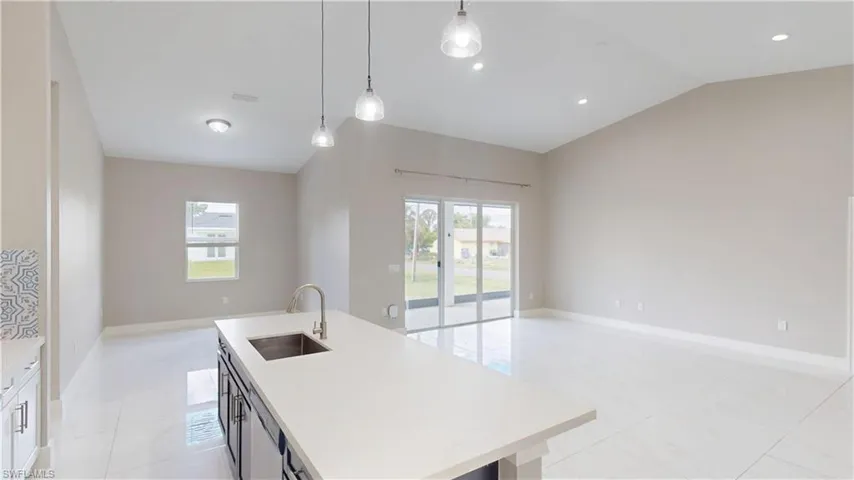 Kitchen with a sink, open floor plan, light countertops, a center island with sink, and decorative light fixtures