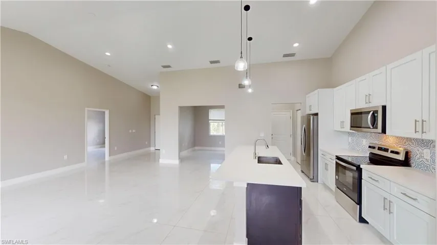 Kitchen with appliances with stainless steel finishes, a sink, high vaulted ceiling, a center island with sink, and light countertops