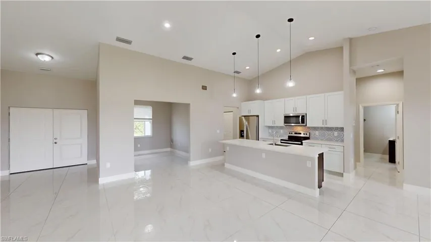 Kitchen featuring stainless steel appliances, a sink, light countertops, an island with sink, and white cabinets