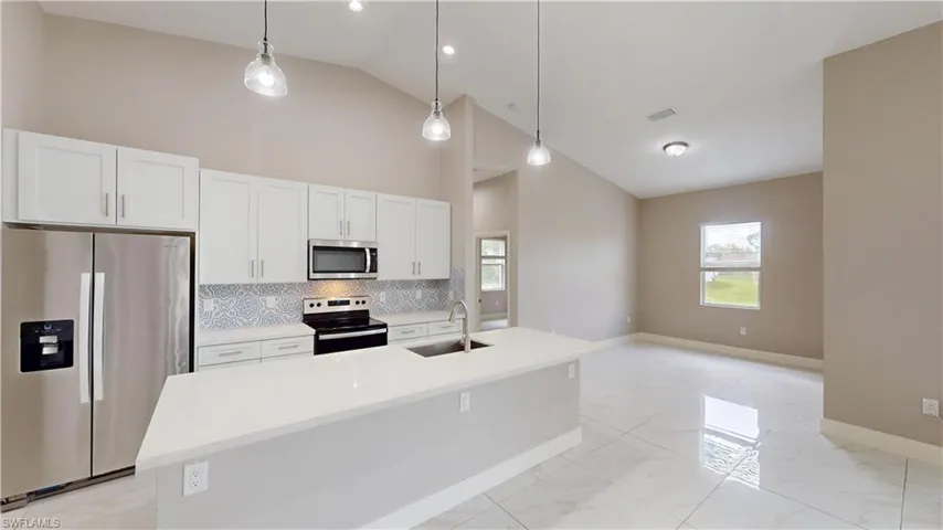 Kitchen with stainless steel appliances, a sink, light marble finish flooring, tasteful backsplash, and white cabinets