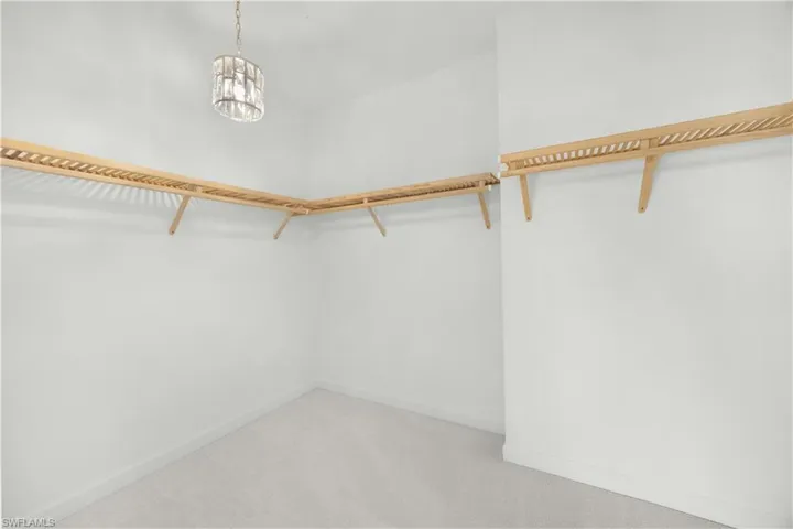 Spacious closet with light colored carpet and a chandelier