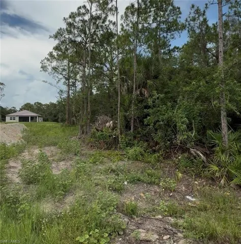 Cleared lot with a distant residence featuring a covered patio and a light-toned exterior