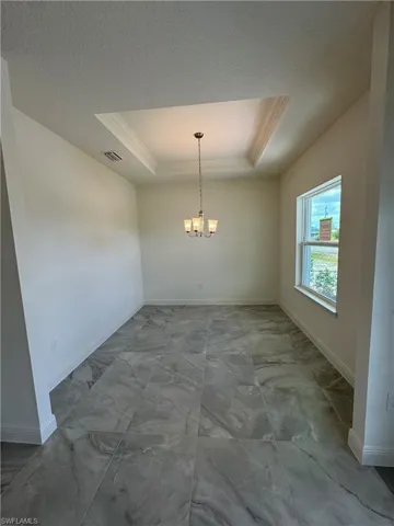 Unfurnished dining area featuring a raised ceiling, marble look tiles, crown molding, a chandelier, and baseboards