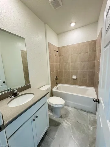 Full bath featuring a textured wall, toilet, vanity, and bathing tub / shower combination