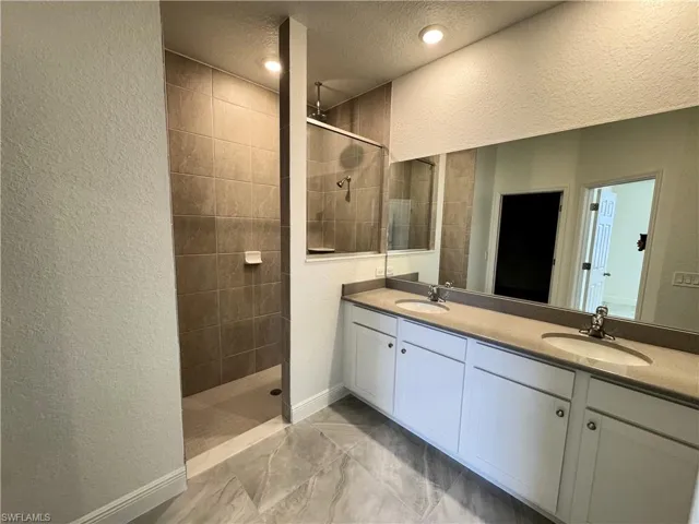 Bathroom with double vanity, walk in shower, a textured ceiling, a textured wall, and baseboards