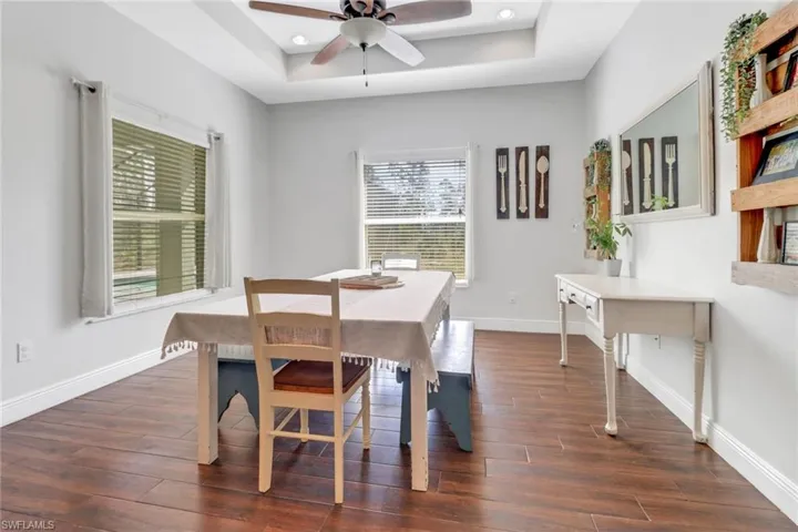 Dining room featuring ceiling fan, baseboards, a tray ceiling, and dark wood-style floors