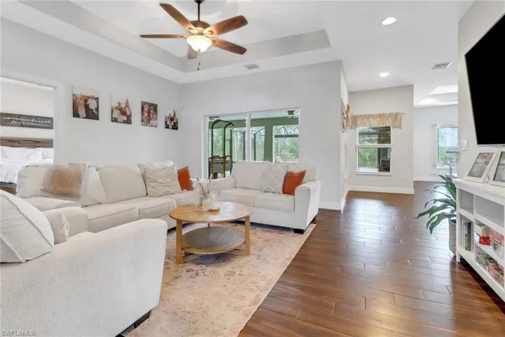 Living room with dark wood finished floors, ceiling fan, a tray ceiling, and visible vents