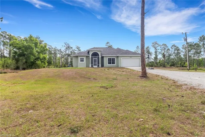 Ranch-style house with an attached garage, gravel driveway, a front lawn, and stucco siding
