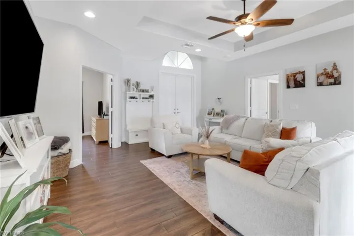 Living area with recessed lighting, a raised ceiling, ceiling fan, and dark wood-style flooring