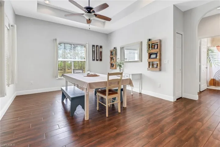 Dining space with a raised ceiling, a ceiling fan, arched walkways, baseboards, and dark wood-style flooring