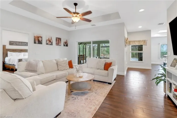 Living room with dark wood-style floors, ceiling fan, a raised ceiling, visible vents, and recessed lighting