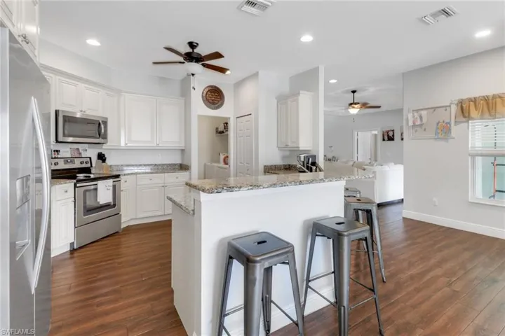 Kitchen with a ceiling fan, appliances with stainless steel finishes, a kitchen bar, dark wood-style flooring, and visible vents