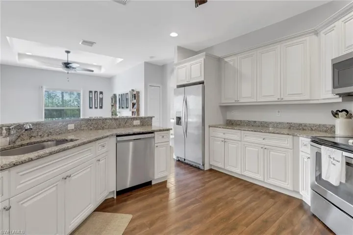 Kitchen featuring a sink, ceiling fan, a tray ceiling, appliances with stainless steel finishes, and recessed lighting