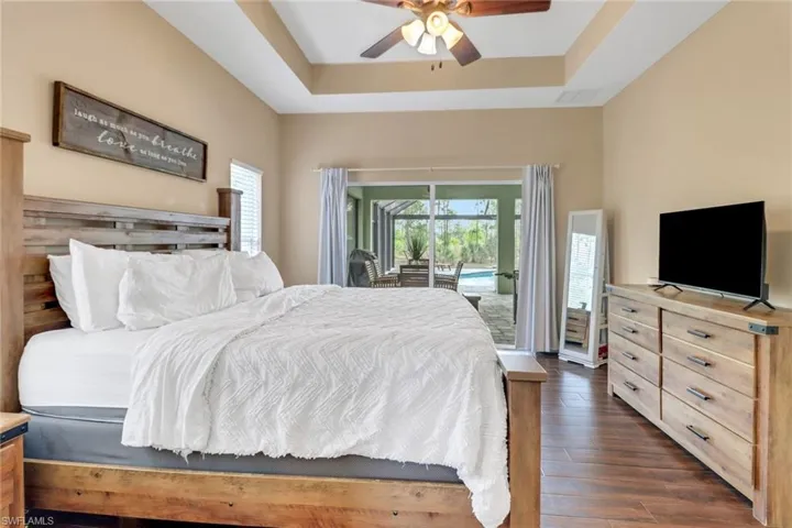 Bedroom with a raised ceiling, visible vents, a ceiling fan, dark wood-type flooring, and access to outside