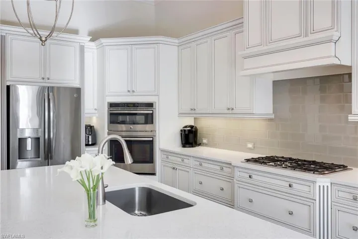 Kitchen featuring stainless steel appliances, white cabinets, quartz countertops, decorative backsplash, and custom range hood