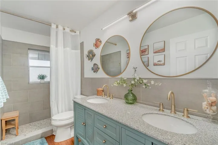 Bathroom with double vanity, a tile shower, tile walls, backsplash, and light wood-type flooring