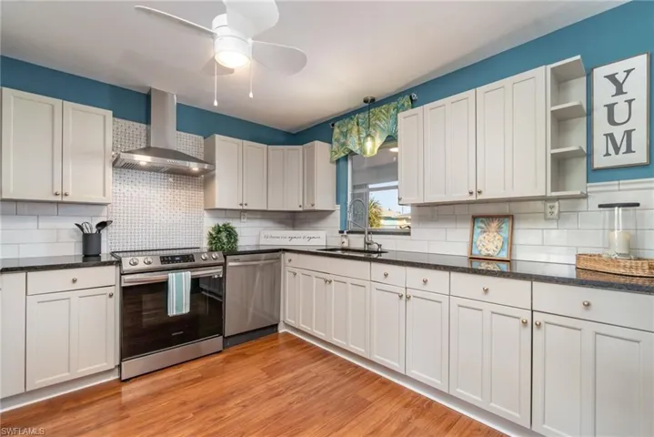 Kitchen featuring stainless steel appliances, white cabinets, wall chimney exhaust hood, and open shelves