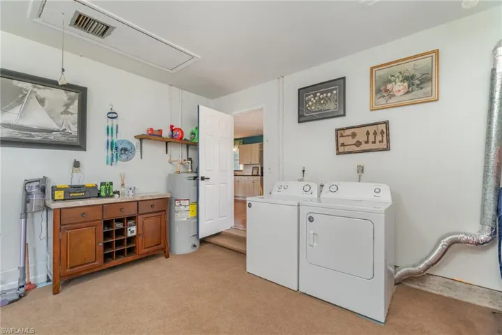 Laundry area in garage featuring attic access, light carpet, electric water heater, and independent washer and dryer