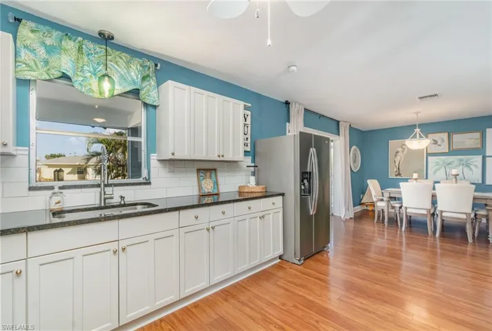 Kitchen with pendant lighting, stainless steel fridge with ice dispenser, white cabinets, light wood-style flooring, and dark stone countertops