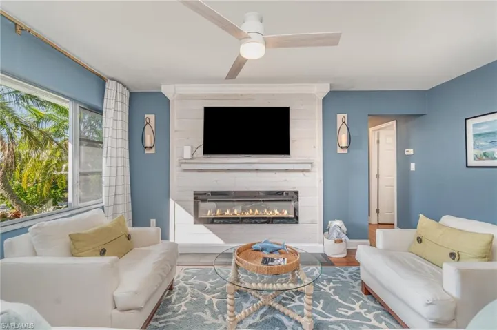 Living area with a large fireplace, a ceiling fan, and wood finished floors