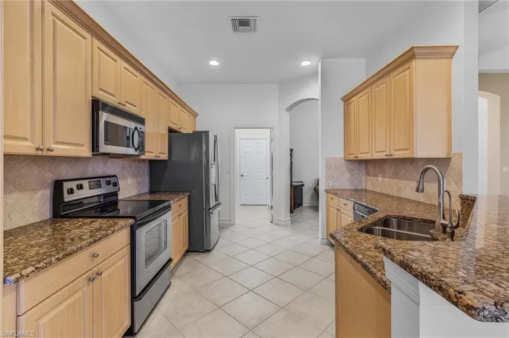 Kitchen with light brown cabinets, sink, stainless steel appliances, and dark stone counters