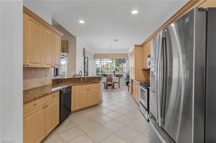 Kitchen with electric range, dishwasher, sink, stainless steel refrigerator with ice dispenser, and dark stone countertops