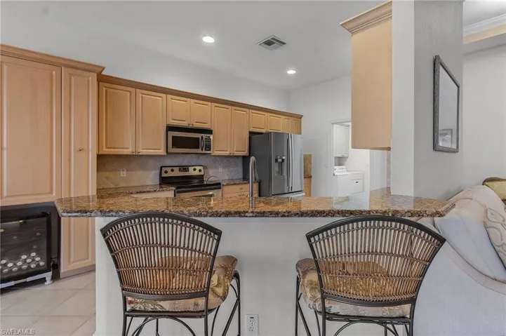 Kitchen featuring washer / dryer, kitchen peninsula, dark stone counters, and appliances with stainless steel finishes
