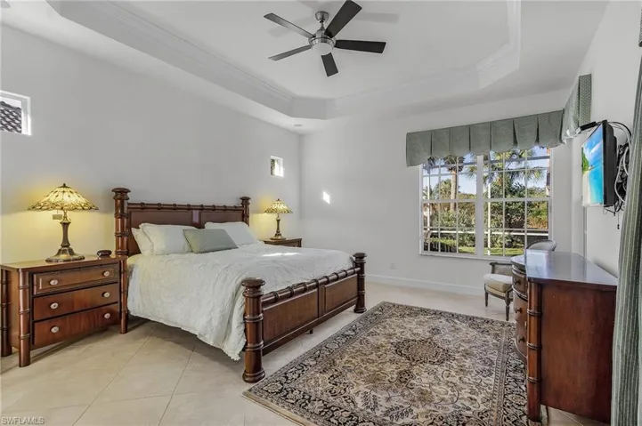 Bedroom with a tray ceiling, ceiling fan, crown molding, and light tile patterned floors