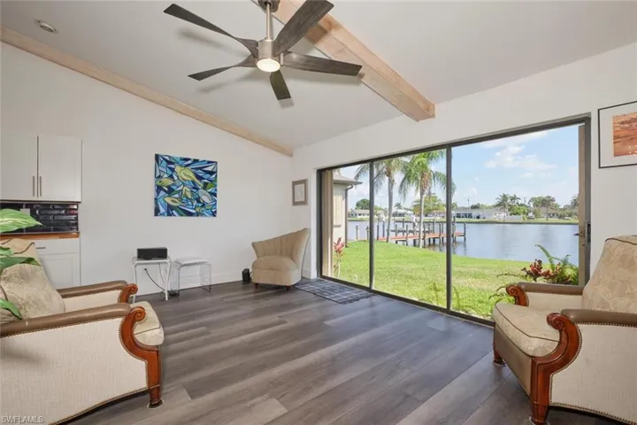Living area featuring vaulted ceiling with beams, a water view, dark hardwood / wood-style flooring, and ceiling fan