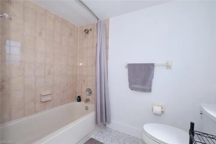 Bathroom featuring shower / bath combo with shower curtain, toilet, and tile floors