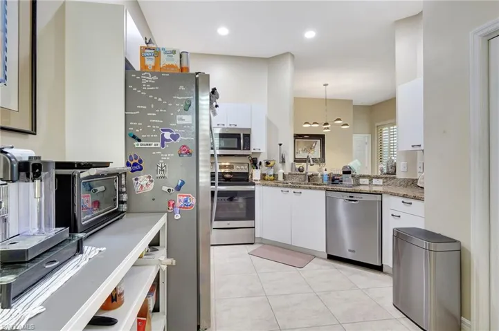 Kitchen featuring light stone countertops, a notable chandelier, white cabinetry, hanging light fixtures, and appliances with stainless steel finishes