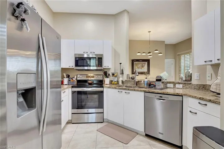 Kitchen with light tile patterned floors, white cabinetry, a sink, appliances with stainless steel finishes, and light stone countertops