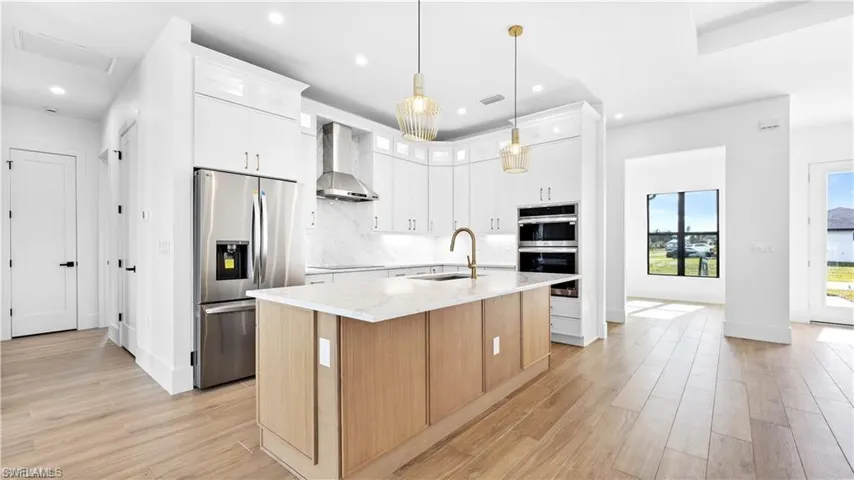 Kitchen with white cabinets, a center island with sink, wall chimney exhaust hood, and appliances with stainless steel finishes