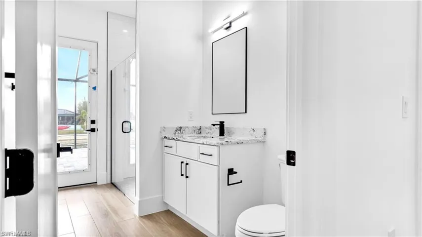 Bathroom with hardwood / wood-style floors, plenty of natural light, a shower with door, and vanity