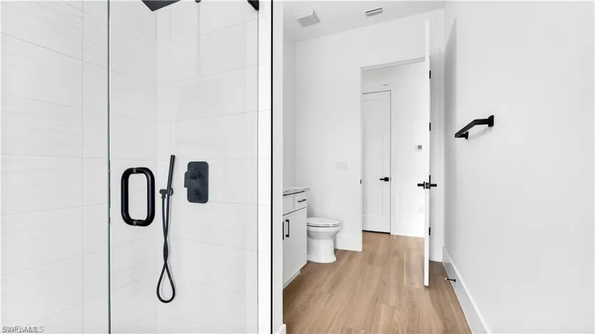 Bathroom featuring hardwood / wood-style floors, vanity, a shower with shower door, and toilet